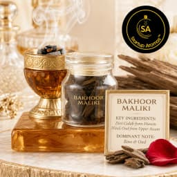 An elegant glass bottle of Bakhoor Maliki incense chips resting on a polished amber block next to a smoking golden chalice, accompanied by raw wood chunks and a soft red rose petal