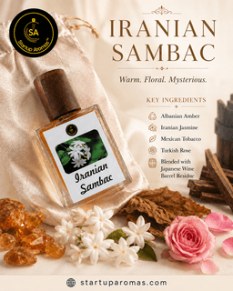 Product display for Iranian Sambac perfume by Startup Aromas. A clear fluted glass bottle filled with rich golden fragrance sits on a smooth marble surface surrounded by fresh white sambac jasmine blossoms, saffron threads, and rose petals against a soft
